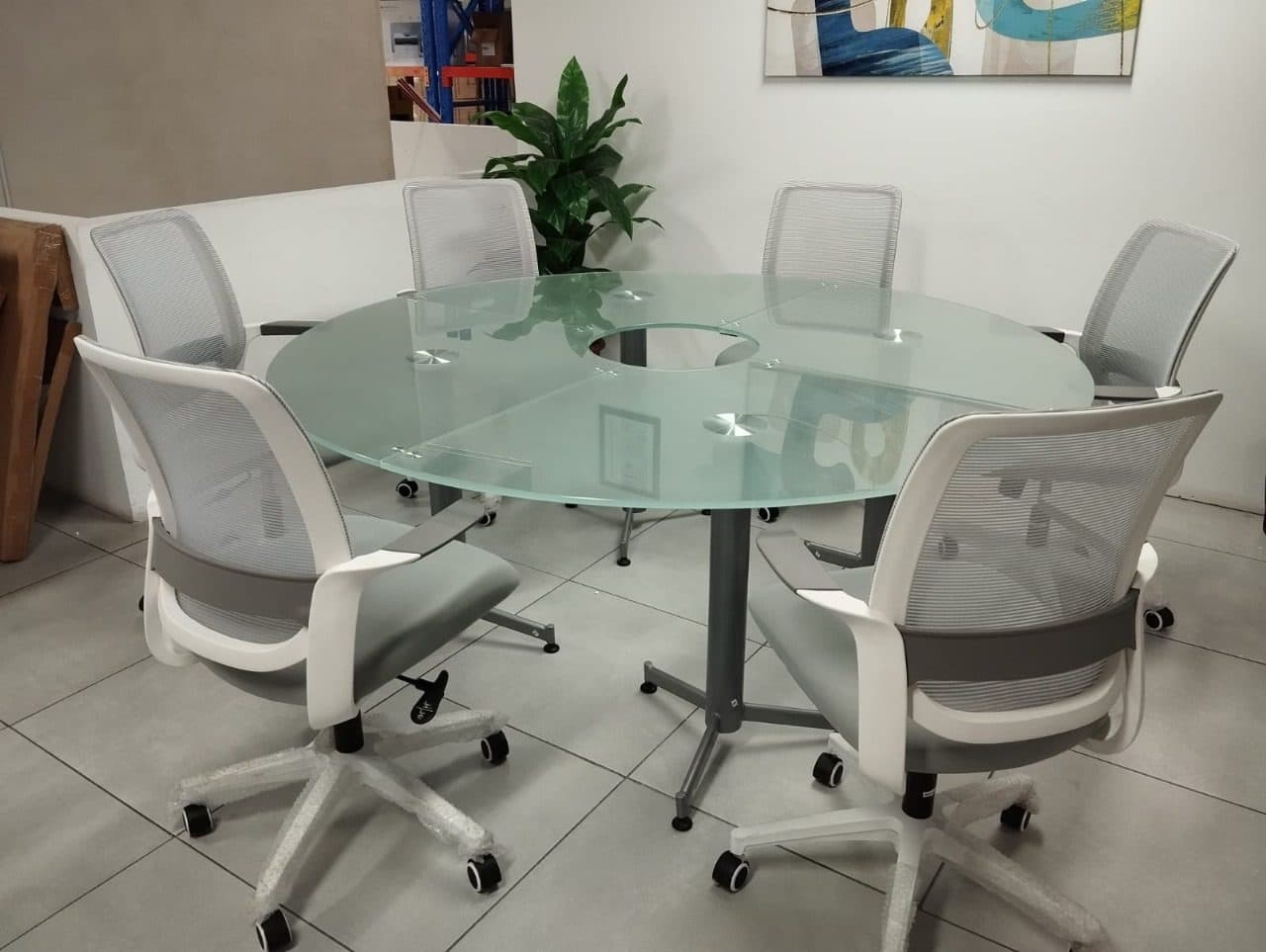 Sala de reuniones pequeña con mesa redonda de vidrio y sillas blancas de malla