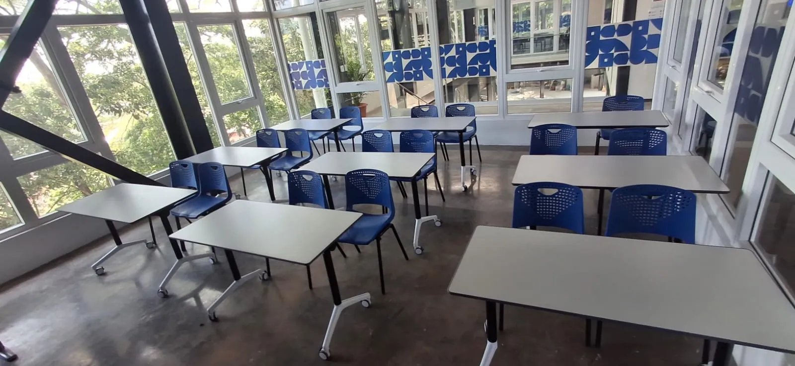 Aula flexible de un campus universitario con mesas plegables sobre ruedas y sillas azules