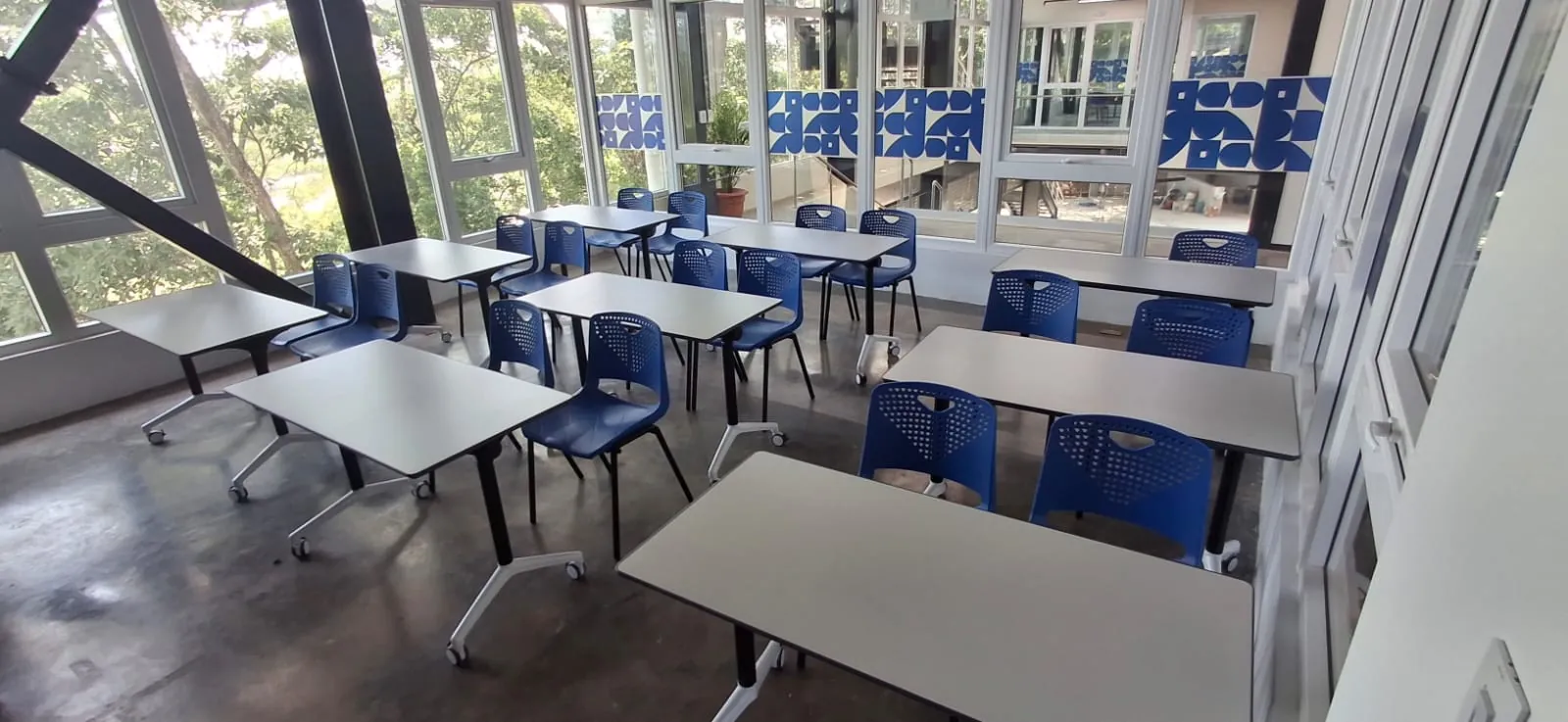 Aula flexible con mesas plegables sobre ruedas y sillas azules frente a un ventanal