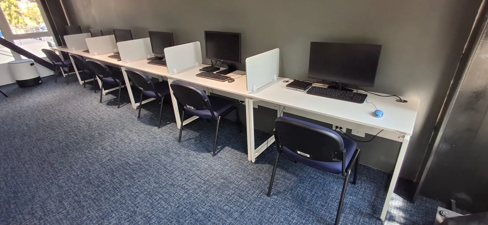 Row of computer desks with low dividers and mesh chairs in a lab