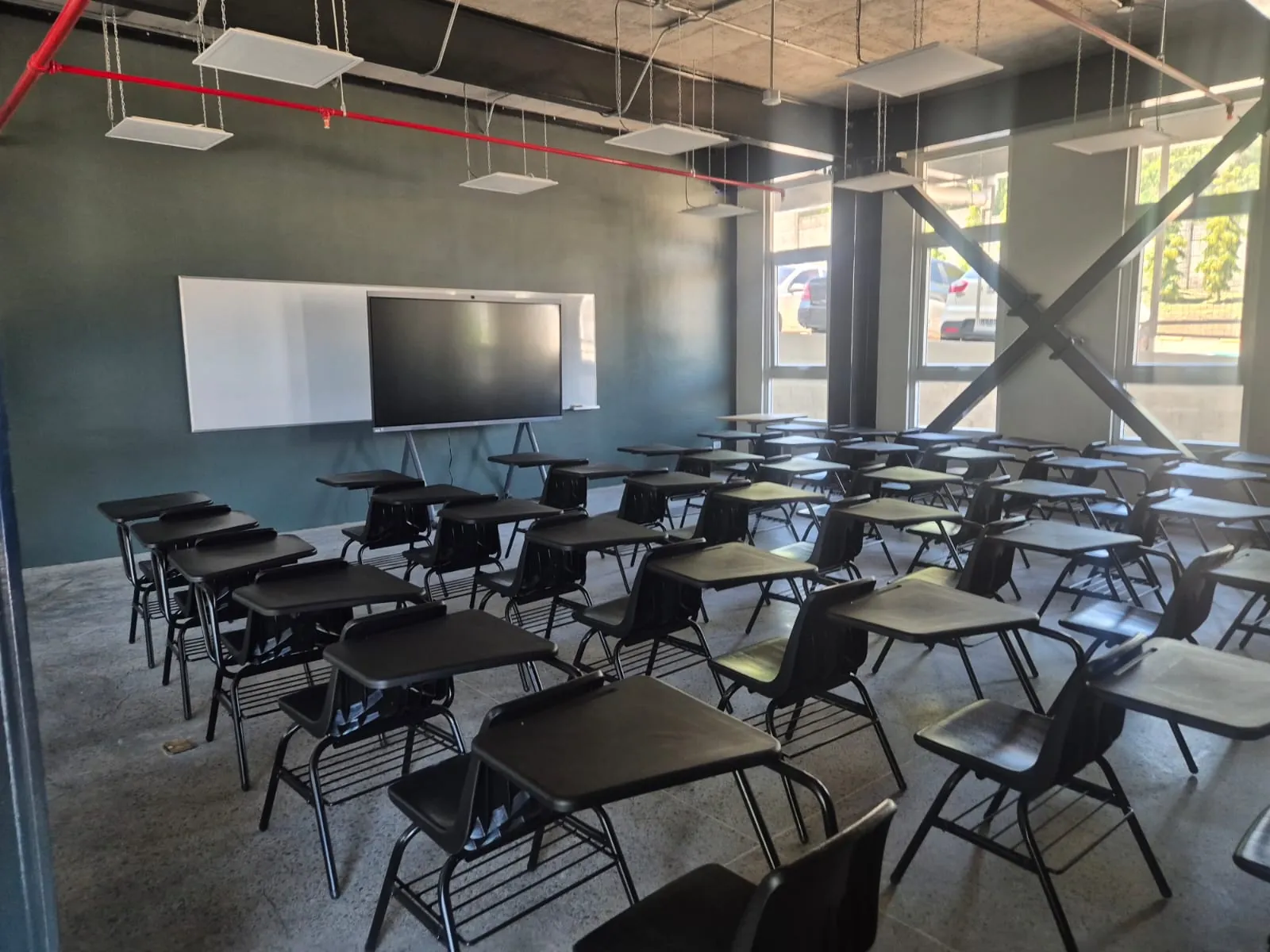 Aula tradicional con sillas de paleta negras en filas frente a una pizarra y una pantalla